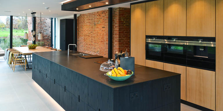 Black veneer handleless island in front of oak veneered floor to ceiling cupboards in this kitchen project in Worcester.